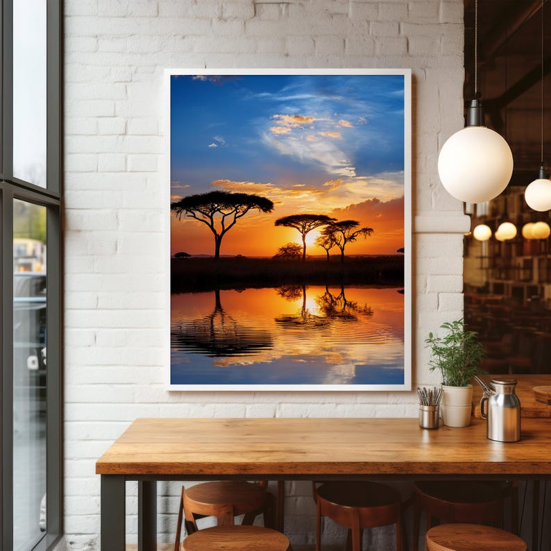 May include: A framed print of an African savanna sunset. The image features silhouetted trees against a vibrant orange and yellow sky, reflected in the still water below. The sky transitions from blue to fiery hues.