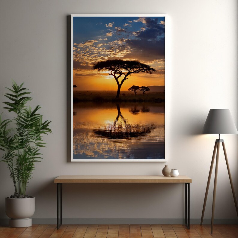 May include: A framed landscape print featuring a vibrant sunset over an African savanna. The image captures a silhouetted tree reflected in calm water, with warm orange and yellow hues dominating the sky and water. The artwork is displayed on a wall.