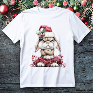 Op de afbeelding: Wit T-shirt met een illustratie van een chagrijnige konijn met een kerstmuts en een rode tutu. Het konijn heeft zijn armen gekruist en is omringd door zuurstokken. Een feestelijk en humoristisch ontwerp.