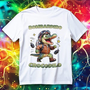Könnte beinhalten: Weißes T-Shirt mit einem Cartoon-Alligator, der einen Pilotenhelm und eine Jacke trägt, mit den Worten "BOMBARDINO CROCODILO". Der Alligator hat eine Rakete und ist von Sternen und Bomben umgeben.