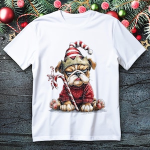 Op de afbeelding: Wit T-shirt met een illustratie van een bulldog die een kerstmuts en trui draagt en een zuurstok vasthoudt. De bulldog heeft een humeurige uitdrukking. Het ontwerp is een gedetailleerde illustratie met een feestelijk thema.
