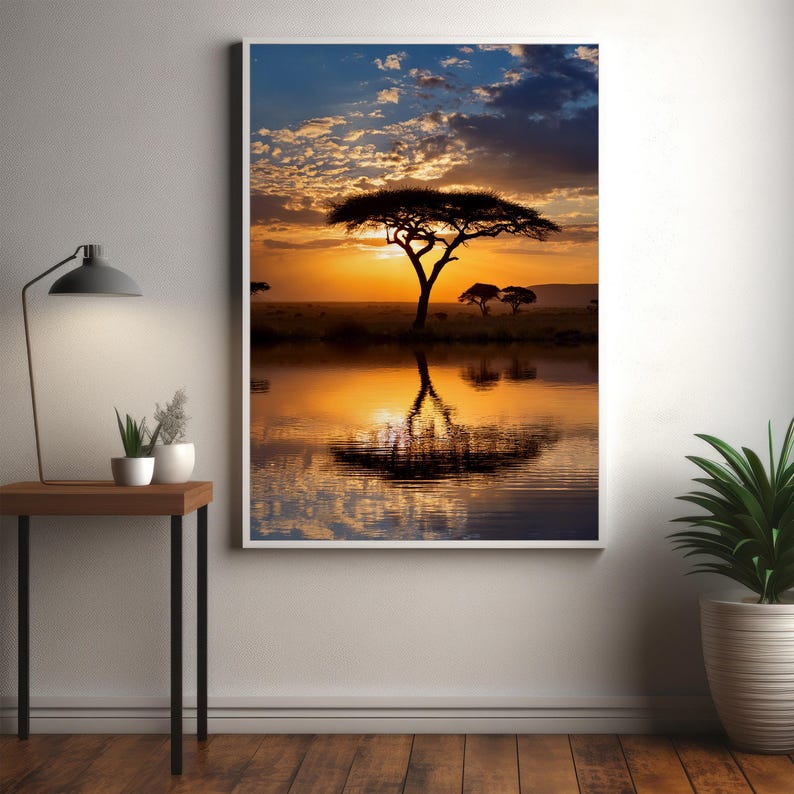 May include: A framed landscape print featuring a vibrant sunset over a tranquil body of water. The image showcases a silhouetted tree, its reflection mirrored in the water. The sky transitions from blue to orange, creating a serene and captivating scene.