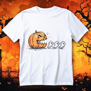 Puede incluir: Camiseta blanca con un diseño de Halloween. Presenta una calabaza naranja sonriente con una boca dentada, seguida de tres pequeños fantasmas blancos. La ilustración tiene un efecto acuarela.