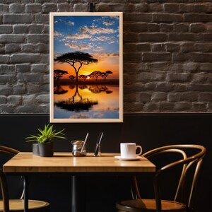 May include: A framed landscape photograph of an African savanna at sunset. The image features silhouetted trees reflected in calm water, with a vibrant orange and yellow sky. The frame is light-colored wood.