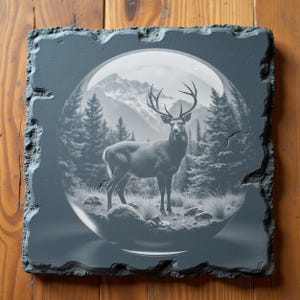 Op de afbeelding: Een vierkante, grijze leistenen tegel met een gedetailleerde gravure van een hert in een glazen bol. Het hert staat in een boslandschap met bergen op de achtergrond. De tegel heeft een ruwe, getextureerde rand.