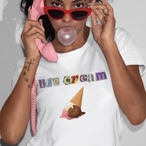 May include: White t-shirt with the text "ice cream" in colourful letters and an ice cream cone graphic. The person in the image is wearing red sunglasses and blowing a bubble. A pink telephone receiver is held to the ear.