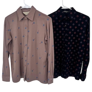May include: Two long-sleeved button-down shirts hanging on a white hanger. One shirt is a mauve color with a repeating blue and red design. The other shirt is navy blue with a repeating floral pattern in red and purple.