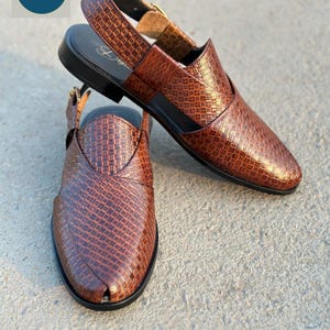 May include: Brown leather sandals with a woven pattern. The sandals have a slingback strap with a buckle closure and a black sole. The word "Saplan" is in a blue circle in the upper left corner.