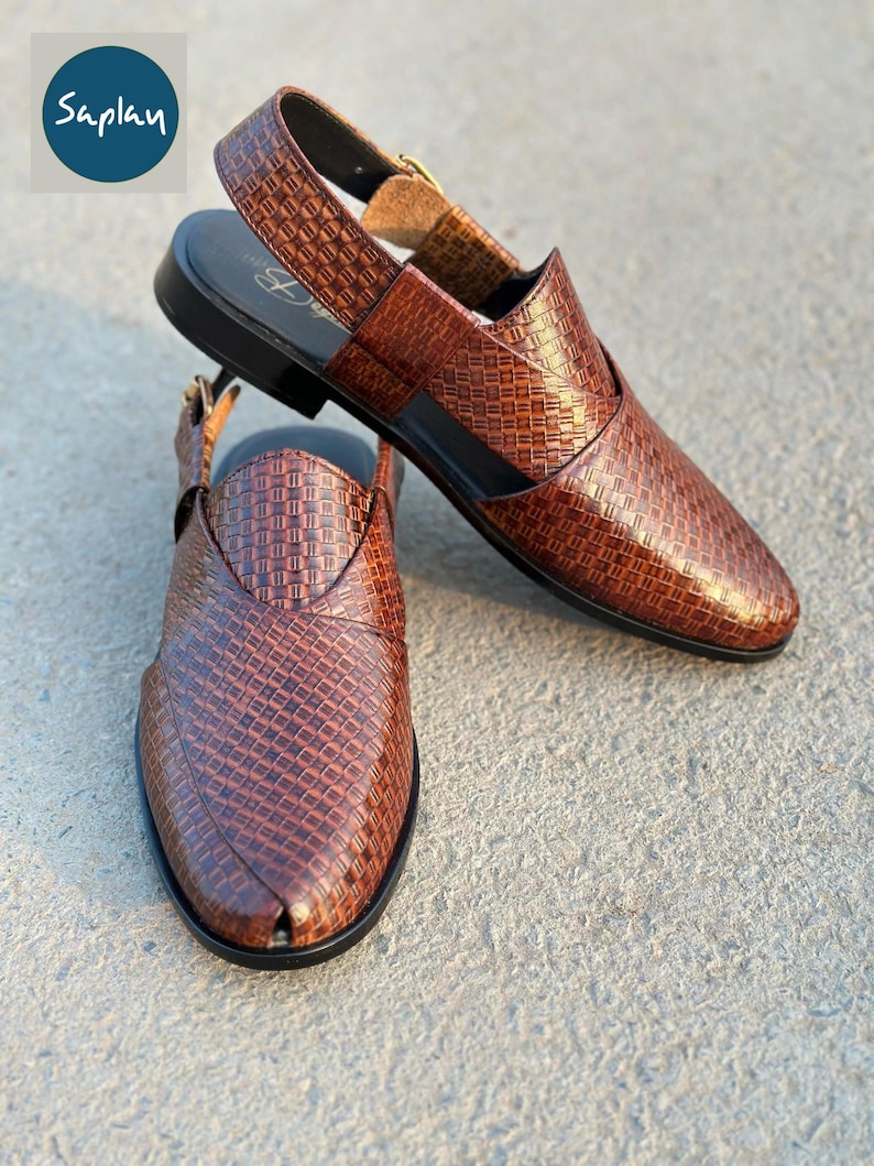 May include: Brown leather sandals with a woven pattern. The sandals have a slingback strap with a buckle closure and a black sole. The word "Saplan" is in a blue circle in the upper left corner.