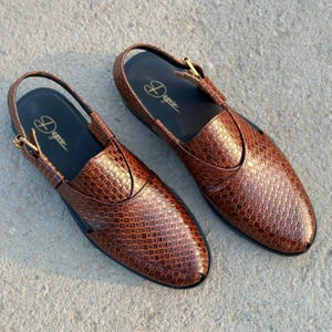 May include: A pair of brown leather sandals with a woven texture. The sandals have a slingback strap and a buckle closure. The brand name "Degere" is printed in gold on the insole. The shoes are displayed on a concrete surface.