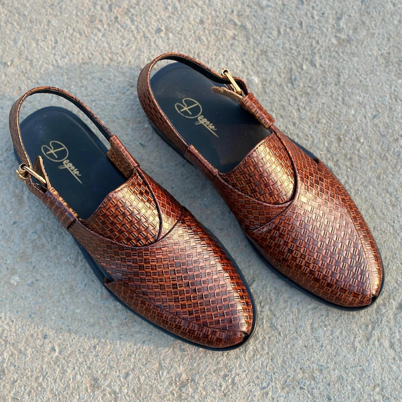 May include: A pair of brown leather sandals with a woven texture. The sandals have a slingback strap and a buckle closure. The brand name "Degere" is printed in gold on the insole. The shoes are displayed on a concrete surface.