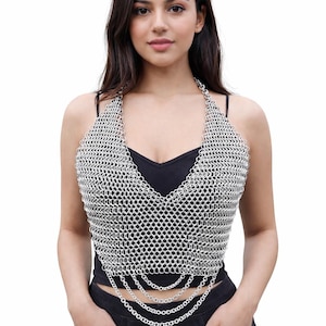 May include: Silver chainmail halter top with a V-neck design. The top features a woven pattern and multiple chain strands hanging from the waist. The model is wearing a black top and black pants.