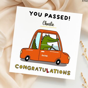May include: A square greeting card with the text "YOU PASSED!" and "CONGRATULATIONS" in yellow and black. The card features an orange car with a green alligator driver. The name "Charlie" is written above the car.