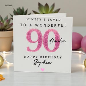 Könnte beinhalten: Eine quadratische weiße Grußkarte mit dem Text NINETY & LOVED TO A WONDERFUL 90 Auntie HAPPY BIRTHDAY Sophia und einem kleinen rosa Herz. Die Zahl 90 ist in einer strukturierten, glitzernden rosa Optik gestaltet. Der Code M1568 steht in der Ecke.