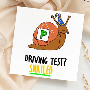 May include: A white greeting card with a cartoon snail wearing a party hat and holding a sign with a green "P". The text reads "DRIVING TEST? SNAILED" in black and yellow. A fun, whimsical design.