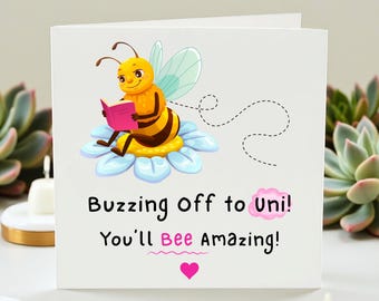 May include: A white greeting card featuring a cartoon bee reading a book, perched on a flower. The card reads "Buzzing Off to Uni! You'll Bee Amazing!" with a pink heart.