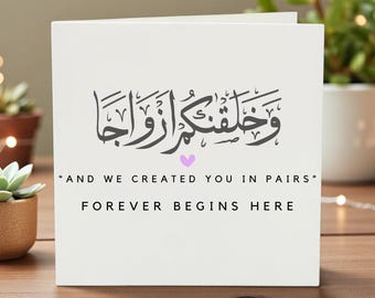May include: A white greeting card with Arabic calligraphy and the English translation "AND WE CREATED YOU IN PAIRS" and "FOREVER BEGINS HERE". A small purple heart is between the phrases. The card is on a wooden surface.