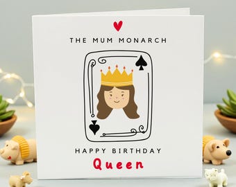 May include: White greeting card with the text "THE MUM MONARCH" and "HAPPY BIRTHDAY QUEEN". The card features a playing card design with a cartoon queen wearing a gold crown. A red heart is at the top.