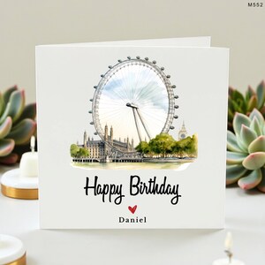 Peut inclure: Carte de vœux blanche avec une illustration à l'aquarelle de la grande roue de Londres et des bâtiments emblématiques. La carte porte l'inscription "Happy Birthday" en écriture noire, un cœur rouge et le nom "Daniel" en dessous.