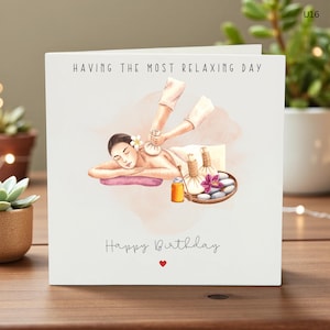 Op de afbeelding: Een witte wenskaart met de tekst "HAVING THE MOST RELAXING DAY" en "Happy Birthday". De kaart toont een illustratie van een persoon die een spabehandeling krijgt, met massagegereedschap en een bloem. Onderaan staat een klein rood hart.
