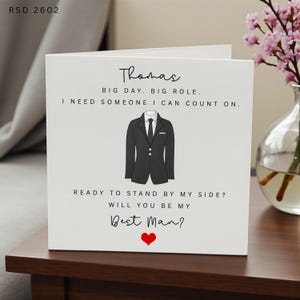 May include: A white greeting card featuring the text Thomas, BIG DAY. BIG ROLE. I NEED SOMEONE I CAN COUNT ON. READY TO STAND BY MY SIDE? WILL YOU BE MY BEST MAN? with a graphic of a black suit jacket and a small red heart at the bottom.