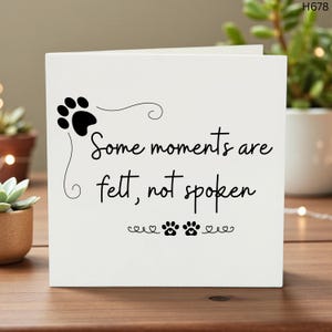 Puede incluir: Tarjeta de felicitación blanca con huella de pata negra y texto: "Algunos momentos se sienten, no se dicen". Presenta huellas de patas y corazones. Ideal para amantes de las mascotas.