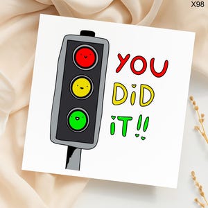 May include: A white greeting card with a cartoon traffic light illustration. The traffic light has a red, yellow, and green light with smiling faces. The words "YOU DID IT!!" are written in red, yellow, and green.