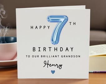Op de afbeelding: Een vierkante witte verjaardagskaart met een groot, metallic blauw cijfer 7 in ballonstijl. De tekst luidt: HAPPY 7TH BIRTHDAY TO OUR BRILLIANT GRANDSON, gevolgd door de naam Henry in cursief schrift en een klein blauw hartje onderaan.