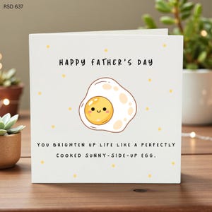 Puede incluir: Tarjeta blanca del Día del Padre con el texto "HAPPY FATHER'S DAY" y una ilustración de huevo de dibujos animados. También incluye el texto "YOU BRIGHTEN UP LIFE LIKE A PERFECTLY COOKED SUNNY-SIDE-UP EGG."