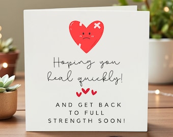 May include: White greeting card with a red heart graphic, stitched with a white cross, and a sad face. The card reads "Hoping you heal quickly!" and "And get back to full strength soon!" in black script.