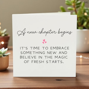 Può includere: Un biglietto bianco con la scritta "A new chapter begins" in corsivo. Sotto, il biglietto recita: "IT'S TIME TO EMBRACE SOMETHING NEW AND BELIEVE IN THE MAGIC OF FRESH STARTS." Cuori rosa adornano il testo. Il biglietto è su una superficie di legno.