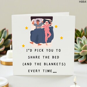 Puede incluir: Tarjeta de felicitación blanca con el texto "I'D PICK YOU TO SHARE THE BED (AND THE BLANKETS) EVERY TIME...". La tarjeta presenta una ilustración de dos personas en la cama, rodeadas de estrellas amarillas.