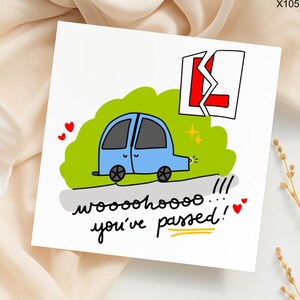 May include: A white greeting card with a cartoon illustration of a light blue car, green grass, and a broken red and white "L" sign. The card has the text "wooohoooo... you've passed!" with hearts.