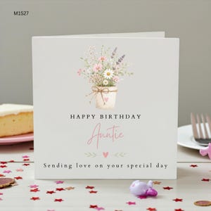 May include: A square white greeting card featuring a watercolor illustration of a potted bouquet of pink and white flowers. The text reads Happy Birthday Auntie, Sending love on your special day, with a small pink heart icon below the bouquet.