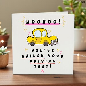 May include: A white greeting card with the words "WOOHOO!" in pink and a yellow cartoon car. Below, it reads "YOU'VE NAILED YOUR DRIVING TEST!" in black text with a red line through "DRIVING".