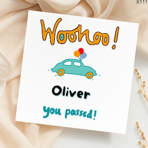 May include: A white card with the words "Woohoo!" in orange, a teal car with balloons, and the name "Oliver" with the text "you passed!" in teal. The card is on a cream-colored surface.
