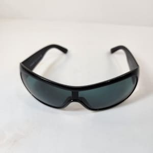 Puede incluir: Gafas de sol envolventes de color negro con un diseño de lente única continua. La montura está fabricada con un material negro sólido con patillas gruesas que se curvan hacia adentro. Las lentes tintadas oscuras cubren todo el rostro.