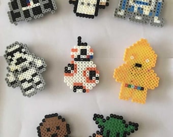 Op de afbeelding: Een verzameling kleurrijke pixel art figuren, waaronder Darth Vader, Princess Leia, R2-D2 en andere personages uit een populaire sciencefiction franchise. Elke figuur is gemaakt van kleine, gesmolten plastic kralen.
