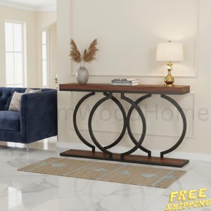 May include: A rectangular console table with a dark wood top and a black metal base featuring two large interlocking circular frames. The table is topped with a white lamp and a stack of books, positioned near a blue sofa and a patterned rug.