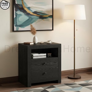 May include: A black wooden nightstand with an open top shelf and two drawers, each featuring a small round knob. Beside the nightstand stands a tall, slender floor lamp with a thin metal pole and a white drum shade, emitting a soft light.