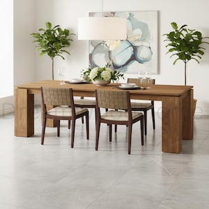 May include: A rectangular wooden dining table with thick block legs and four chairs featuring dark wood frames, woven tan backrests, and off-white upholstered seats. The table is set with white plates, clear glassware, and a central white floral arrangement.