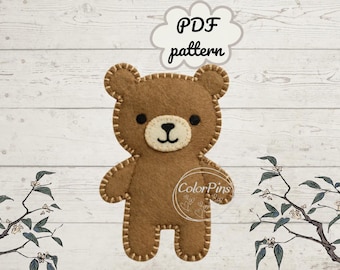 May include: A brown felt bear cutout with a cream-colored muzzle, black eyes, and a stitched nose and mouth. The bear features visible light-colored blanket stitching along its edges. Above the bear is a cloud-shaped graphic with the text PDF pattern.