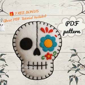 May include: A white felt sugar skull ornament featuring black stitched details, a solid black eye socket, and a blue and yellow flower design on the other side. The text reads FREE BONUS Ghost PDF Tutorial Included and PDF pattern.