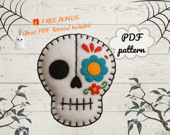 May include: A white felt sugar skull ornament featuring black stitched details, a solid black eye socket, and a blue and yellow flower design on the other side. The text reads FREE BONUS Ghost PDF Tutorial Included and PDF pattern.