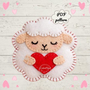 May include: A felt sheep holding a red heart. The sheep has a white body, tan face and ears, and closed eyes. The image includes the text "PDF pattern" in a cloud-shaped speech bubble. The sheep is surrounded by pink hearts.
