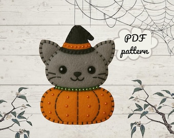 Puede incluir: Un gato de fieltro gris con un sombrero de bruja sentado sobre una calabaza naranja. El gato tiene una cara sonriente y bigotes. La calabaza está decorada con cuentas naranjas. La imagen incluye el texto "PDF pattern".