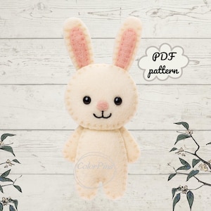 May include: A cream-colored felt bunny with pink inner ears, black eyes, and a stitched smile. The bunny is standing upright. Text in a cloud bubble reads "PDF pattern". The background is a white wood grain.