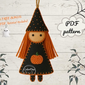 Puede incluir: Un adorno de muñeca de fieltro con un sombrero de bruja negro con puntos naranjas, cabello largo de lana naranja y un vestido negro decorado con una calabaza de cuentas naranja. La muñeca tiene cara beige con ojos negros y una cuerda para colgar.