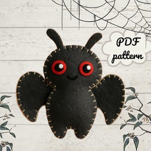 Puede incluir: Una polilla de fieltro negro con ojos rojos y costuras beige. La polilla tiene dos antenas y dos alas. El texto "PDF pattern" está en una burbuja blanca. Telaraña y elementos florales en el fondo.