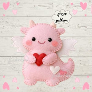 May include: A pink felt dragon holding a red heart, with white wings and a white heart on its tail. The dragon has black eyes and a smiling face. The image includes the text "PDF pattern" in a cloud-shaped speech bubble.